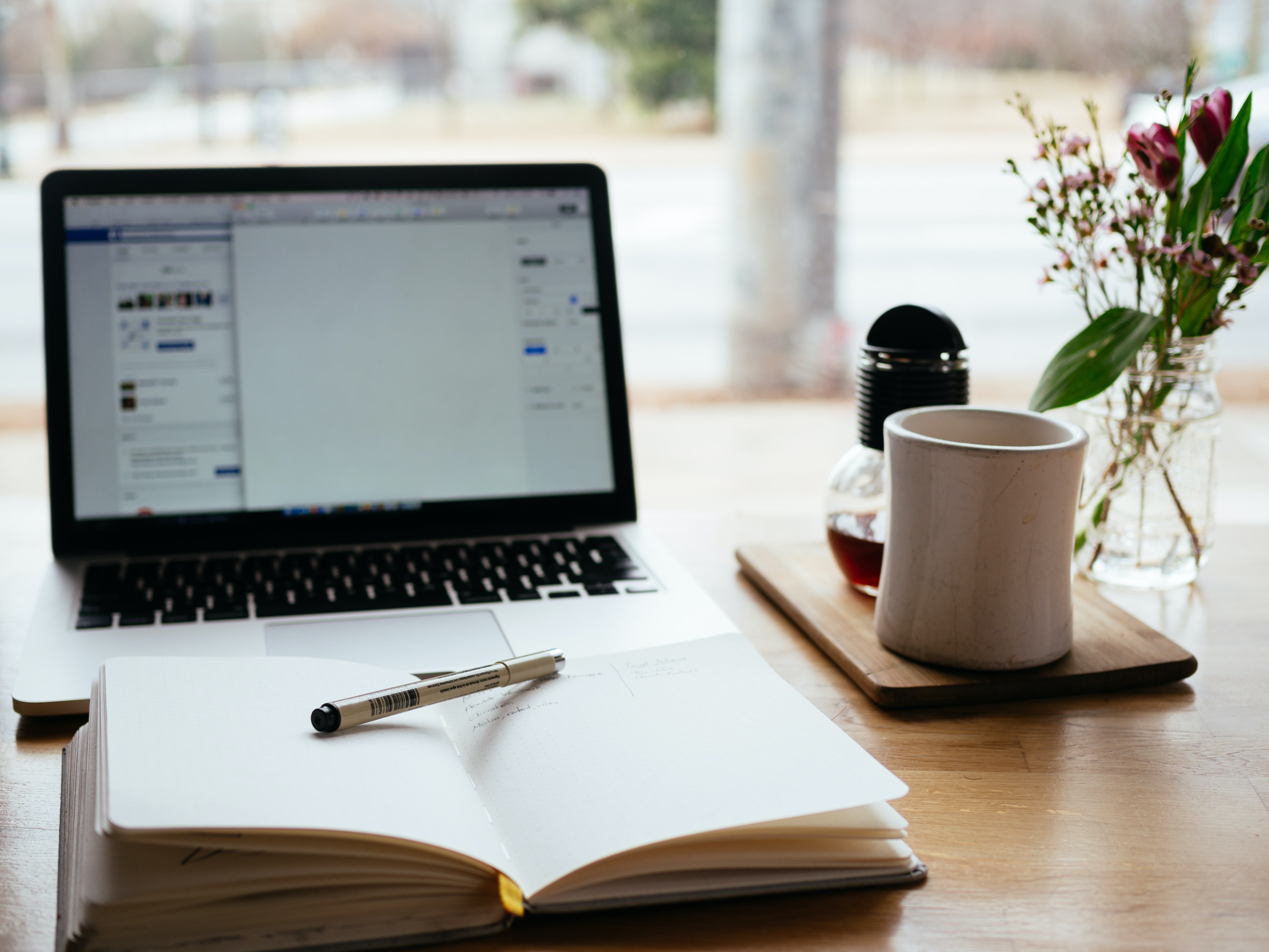 A picture of a laptop with an open notebook and pen, and coffee at the side.