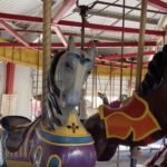 An image of the Roswell Carousel at the Spring River Zoo in Roswell, NM. There are two leaping horses, a chicken, and a deer.