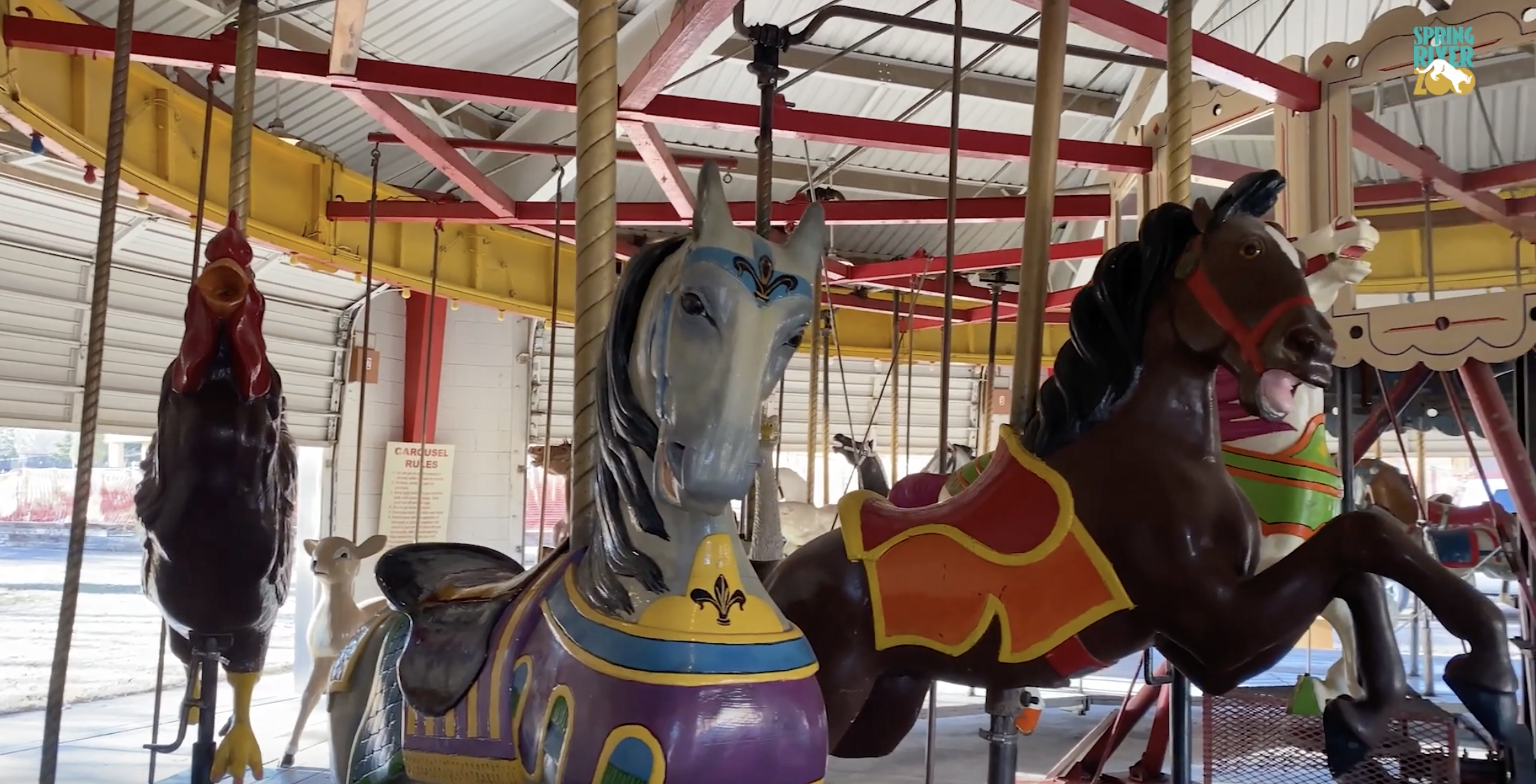 An image of the Roswell Carousel at the Spring River Zoo in Roswell, NM. There are two leaping horses, a chicken, and a deer.