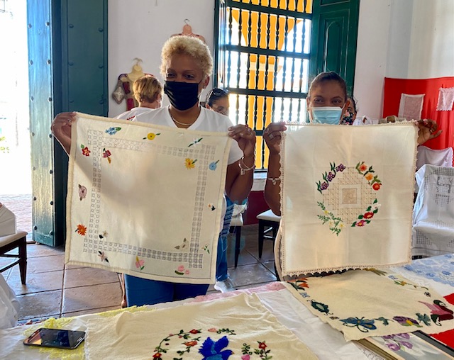 Obdulia Gonzalez and Zobeida Gonzalez are pictured in Trinidad, Cuba showing their needle work pieces that will be finished by Santa Fe’s artisans. In the foreground on the table are the colcha embroidery pieces delivered from the Santa Fe artisans.