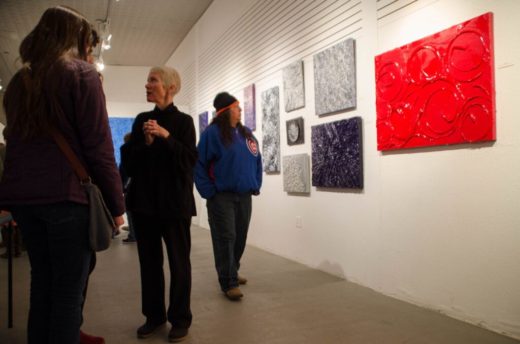 Several people attend the gallery show of artist Linda Bowlby, who creates 3D paint patterns on a canvas.