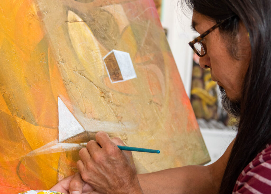 Closeup on the face and hands of artist Jerry Brown as he paints on a canvas.