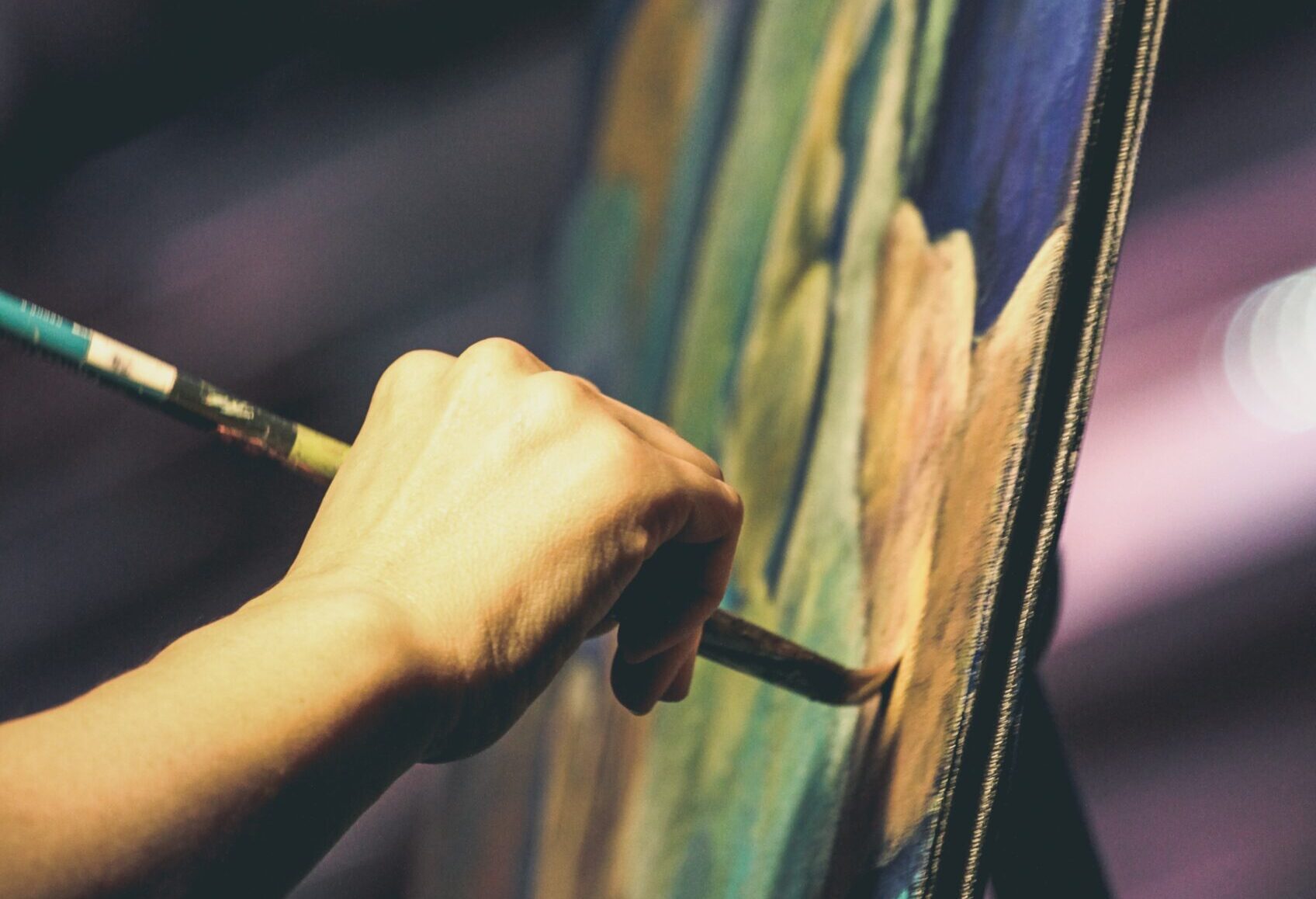 Closeup on the hand of a painter as they brush paint onto an easel.